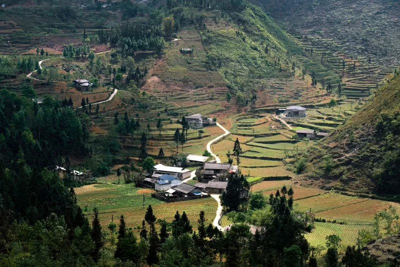 Aerial view of a mountain village with terraced fields and winding roads in Ha Giang.