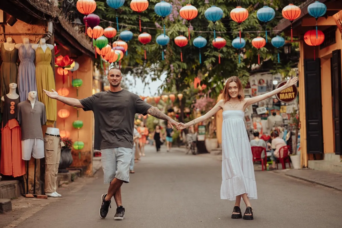A couple holds hands under colorful lanterns on a lively street in Hoi An's old town.
