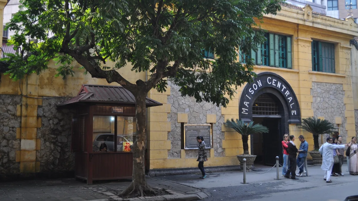 Visitors gather at the yellow entrance gate of Hoa Lo Prison, marked 'Maison Centrale', in Hanoi.