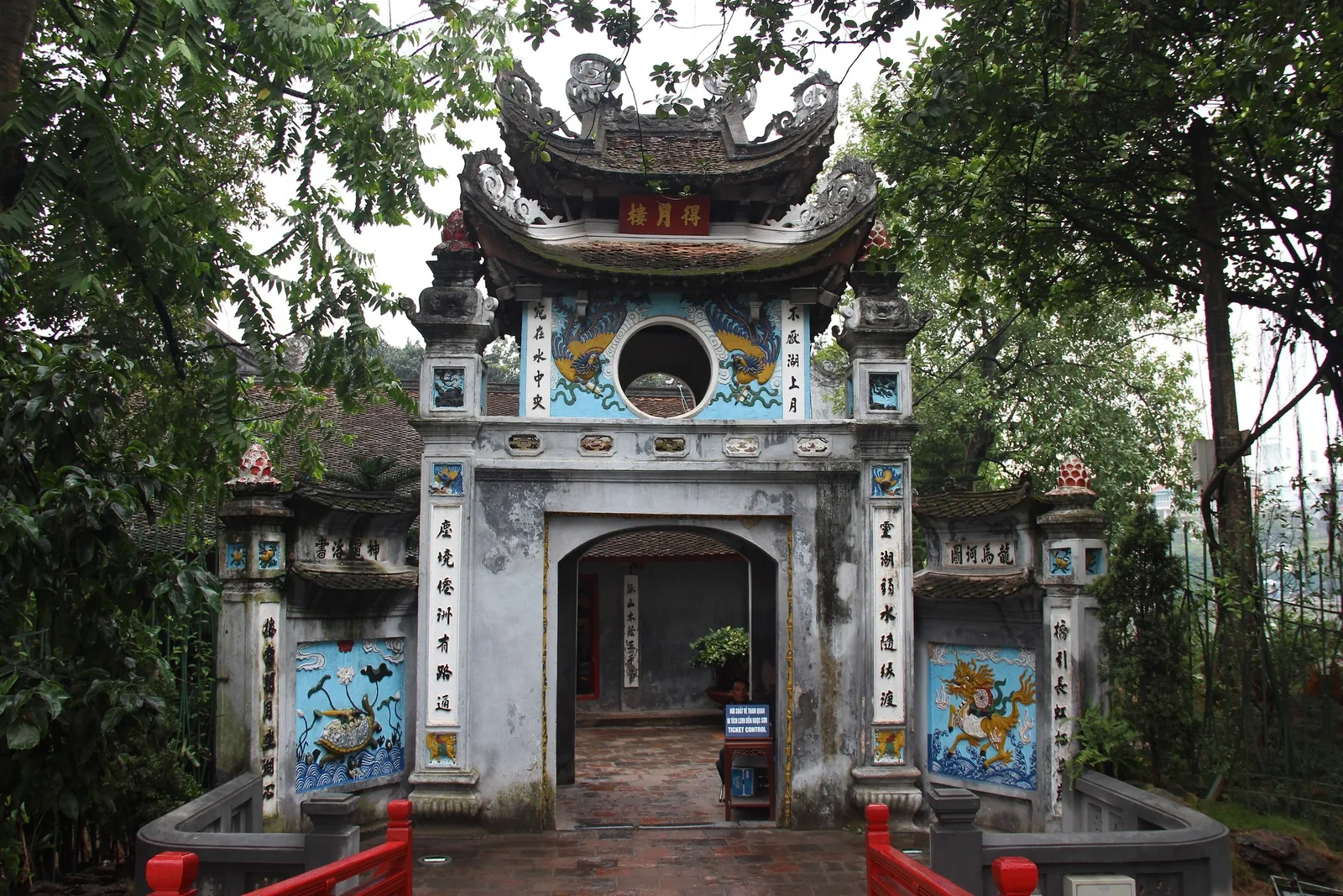 Ornate gate with dragon carvings and a red bridge leads into Ngoc Son Temple in Hanoi.