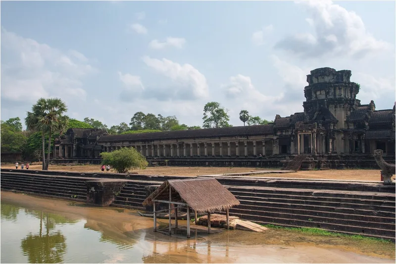 A stone gallery and tower of Angkor Wat rise beyond a moat lined with steps in Siem Reap.