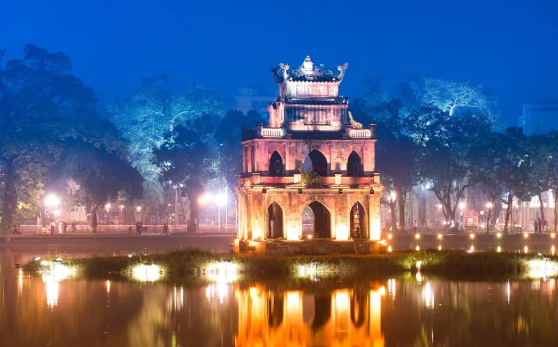 Turtle Tower illuminated at night reflecting on Hoan Kiem Lake in Hanoi