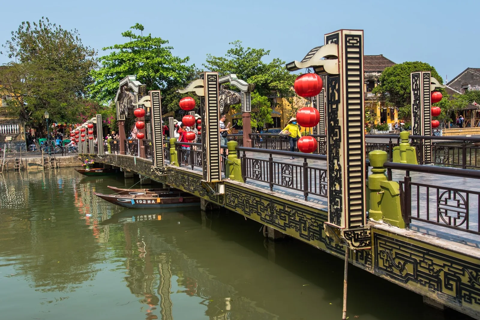 Red lanterns hang along an ornate pedestrian bridge over the river in Hoi An's old town.