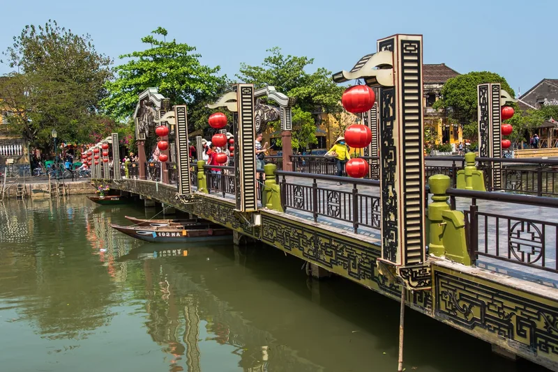Red lanterns hang along an ornate pedestrian bridge over the river in Hoi An's old town.