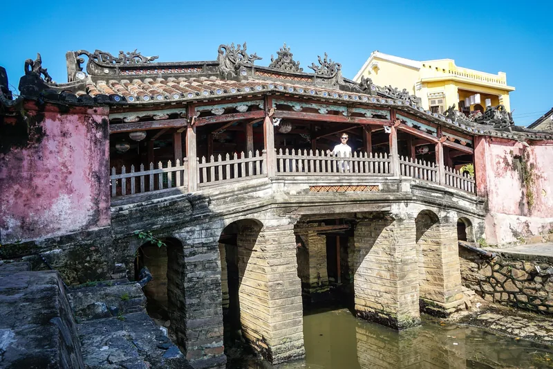 A visitor stands atop the covered Japanese Bridge with its ornate tiled roof in Hoi An's old town.