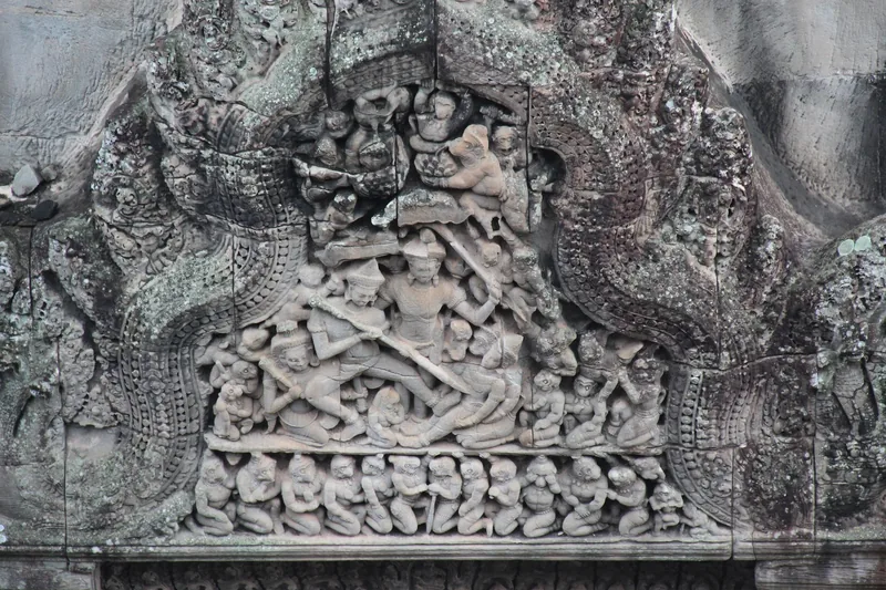 Weathered sandstone lintel carving depicting figures and mythical scenes at an Angkor temple in Siem Reap.