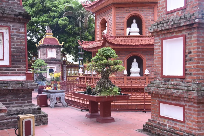Red-brick pagoda towers with Buddha statue niches and bonsai trees at a temple courtyard in Hanoi.