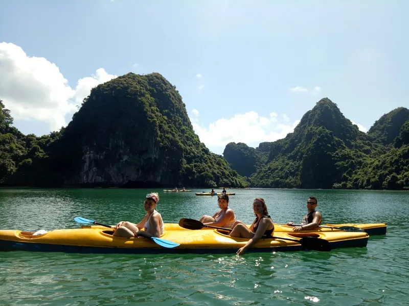 Tourists in yellow kayaks paddle among limestone karsts on the emerald waters of Lan Ha Bay.