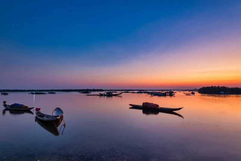Small wooden fishing boats float on the calm waters of Tam Giang Lagoon under a vivid sunset sky.