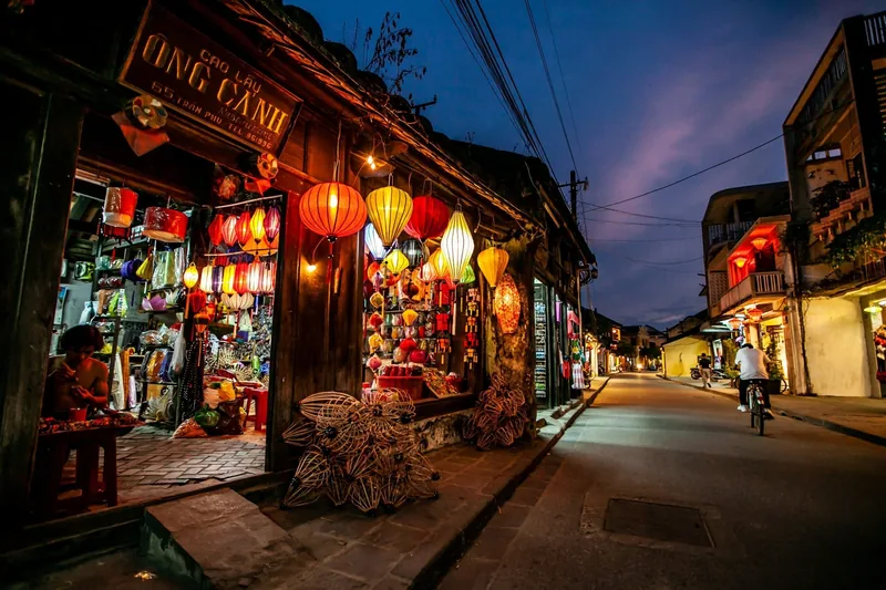 Colorful silk lanterns light a shopfront on a quiet evening street in Hoi An's old town.