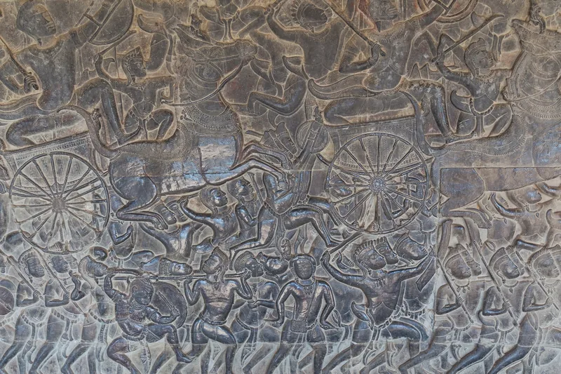 A detailed stone bas-relief depicts warriors, chariots and battle scenes on a wall at Angkor Wat, Siem Reap.