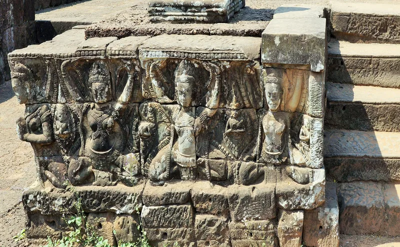 Weathered stone carvings of deities line a temple staircase base in Siem Reap, Cambodia.