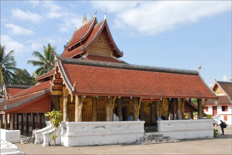 Ornate red-roofed Buddhist temple with gilded columns and multi-tiered eaves in Luang Prabang.