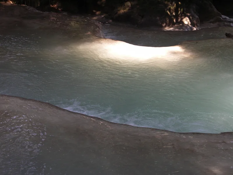 Turquoise water flows over limestone tiers at Kuang Si Falls near Luang Prabang.