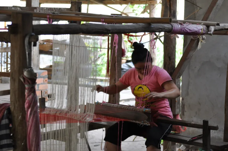 A woman works a traditional wooden loom, weaving colorful threads in a workshop near Luang Prabang.