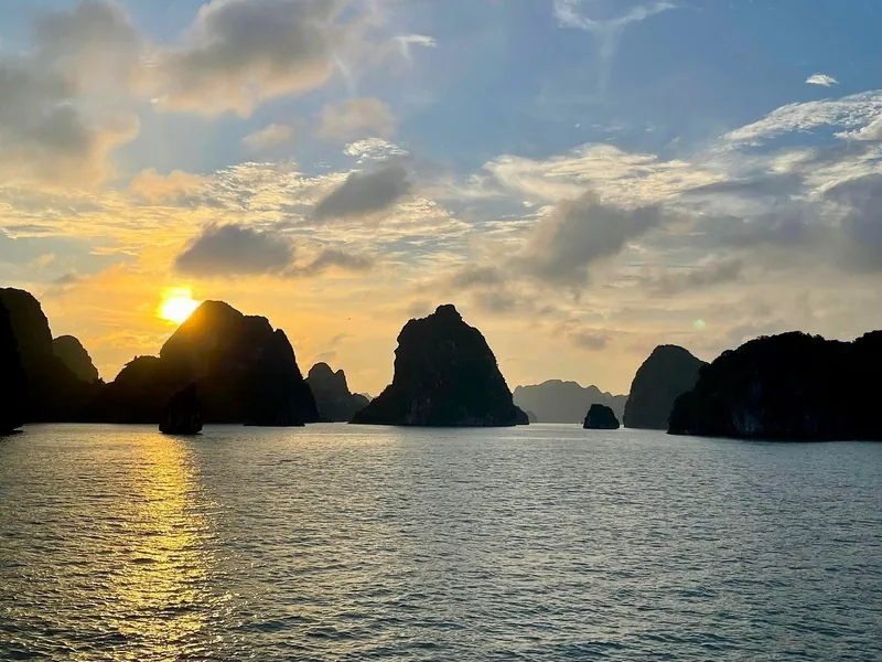 Sun sets behind silhouetted limestone karsts rising from the calm waters of Lan Ha Bay near Cat Ba