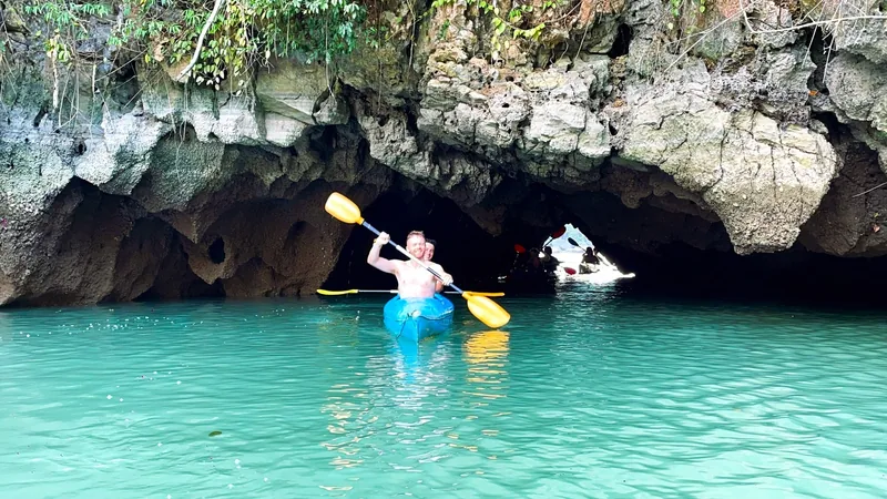 A man paddles a kayak through a limestone cave with turquoise water in Lan Ha Bay.