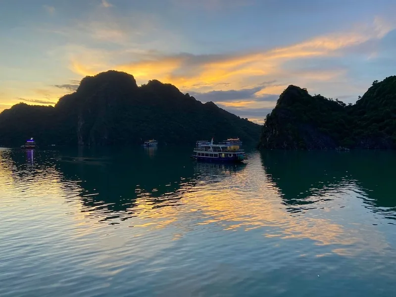 Cruise boats drift among limestone karsts under a golden sunset in Lan Ha Bay near Cat Ba.