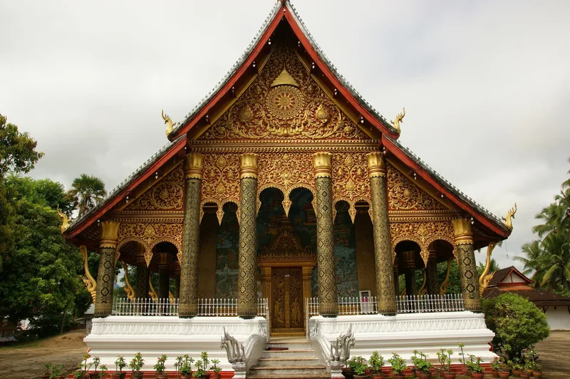 An ornate golden temple facade with red steep roofs at Wat Mahathat in Luang Prabang, Laos.