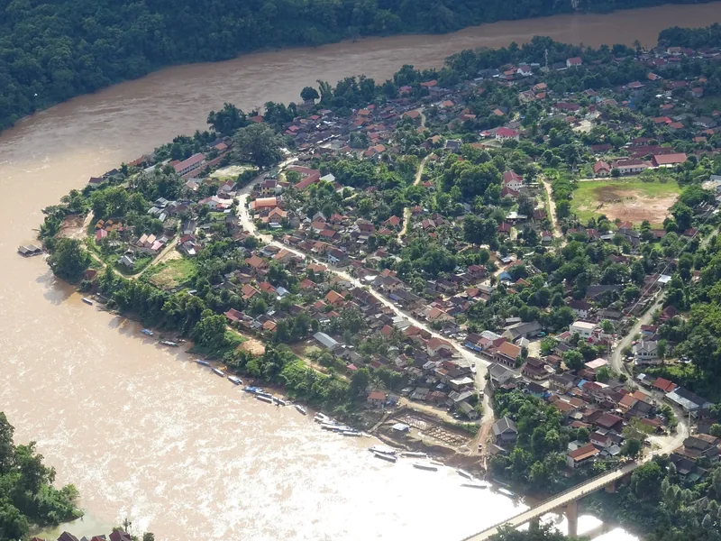 Aerial view of Nong Khiaw town nestled on a bend of the muddy Nam Ou river surrounded by forested hills.