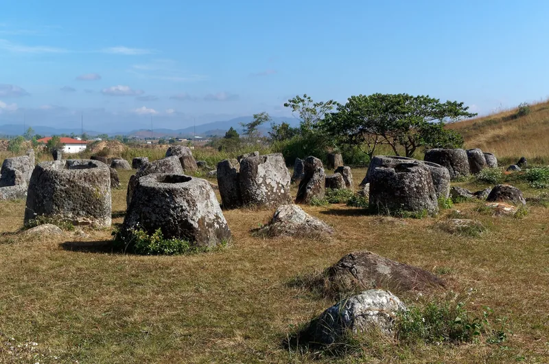 Ancient stone jars scattered across a grassy field at the Plain of Jars in Laos.