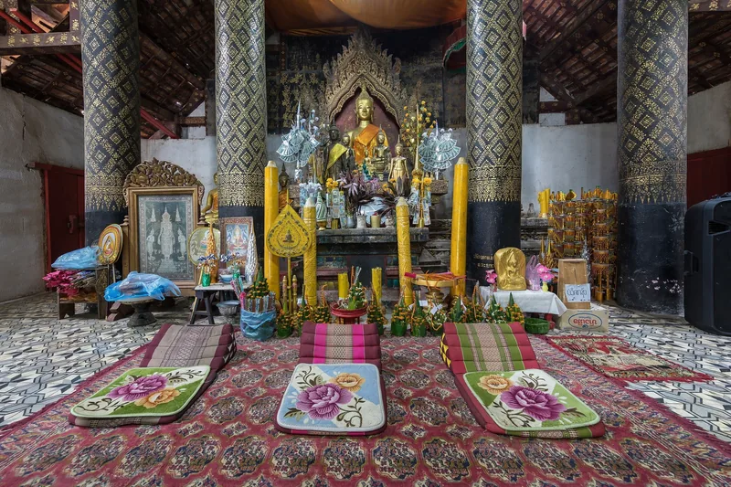 Prayer mats and golden candles face a gilded Buddha altar inside a temple in Luang Prabang, Laos.