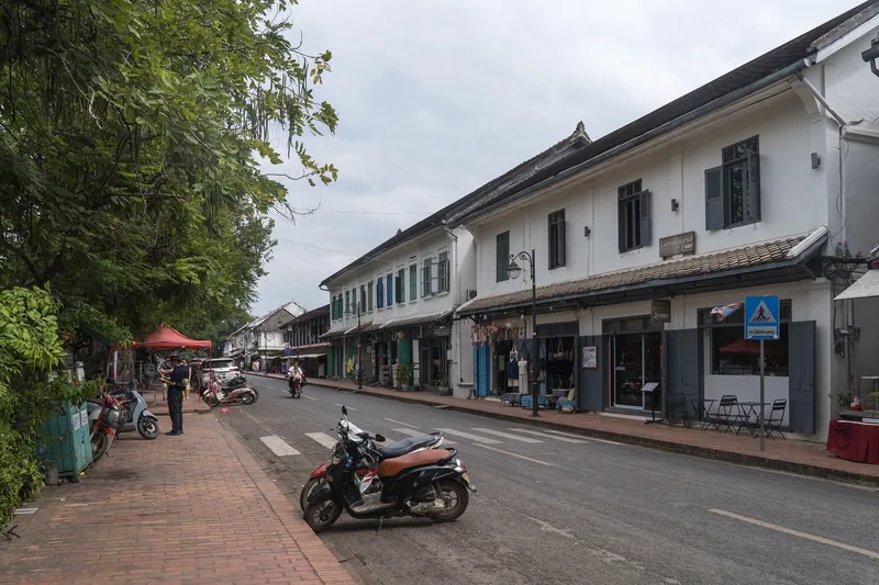 Colonial-style shophouses line a quiet street in Luang Prabang with a parked motorbike in the foreground.