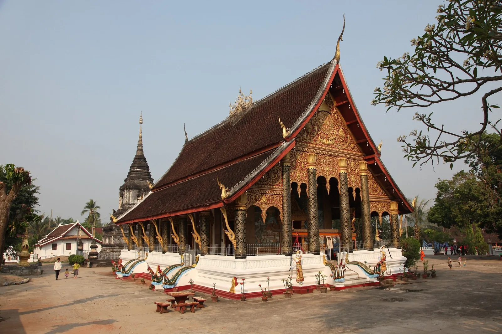 A golden-gabled temple with a steep tiered roof stands beside a stupa at Wat Mahathat in Luang Prabang.