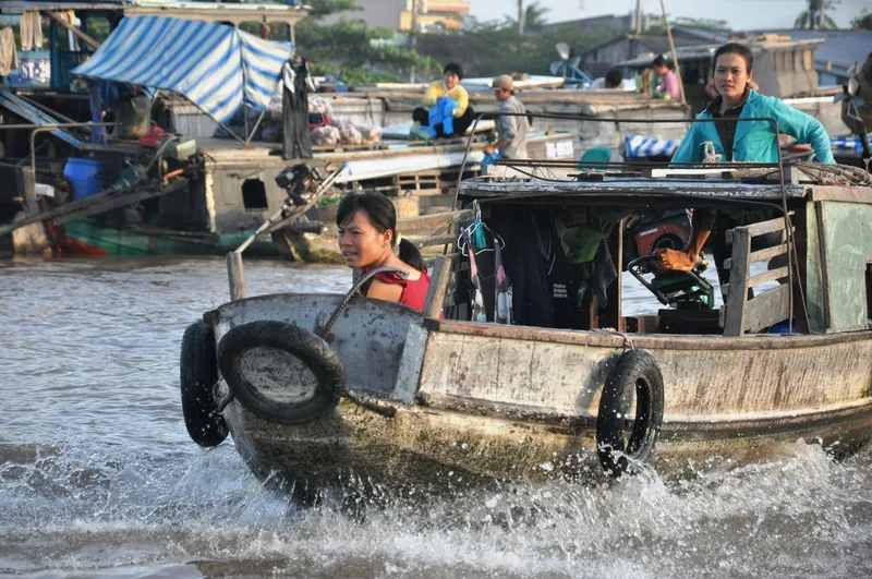 Women steer a wooden boat through splashing water at Cai Rang floating market near Can Tho.