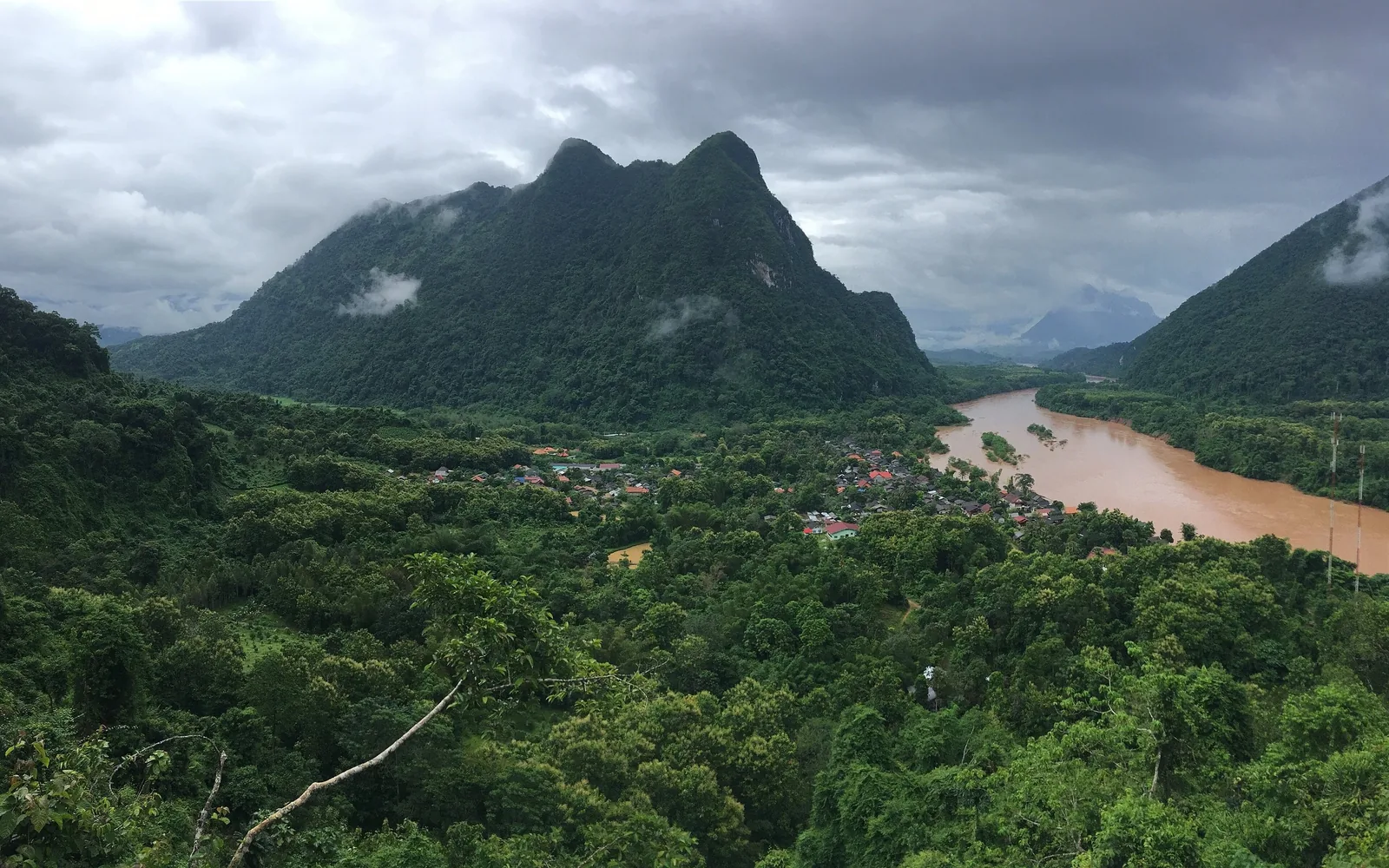 A muddy river winds past a small village nestled among limestone peaks near Nong Khiaw, Laos.