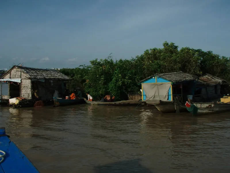 Floating houses and wooden boats line a muddy river near Siem Reap, Cambodia.