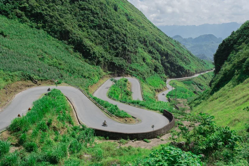 A winding S-shaped road curves through green mountains in Ha Giang province.