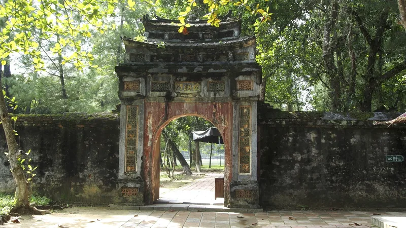 An old ornate stone gate leads into the shaded grounds of the Tomb of Emperor Minh Mang in Hue.