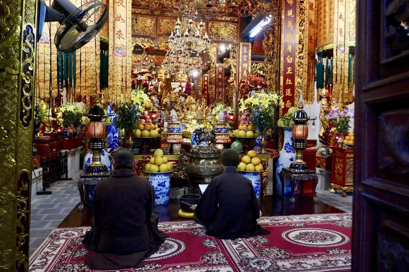 Two monks kneel in prayer before an ornate golden altar inside a temple in Hanoi.