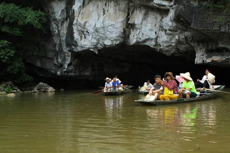 Small boats carry tourists through a limestone cave entrance on the river at Trang An, Ninh Binh.