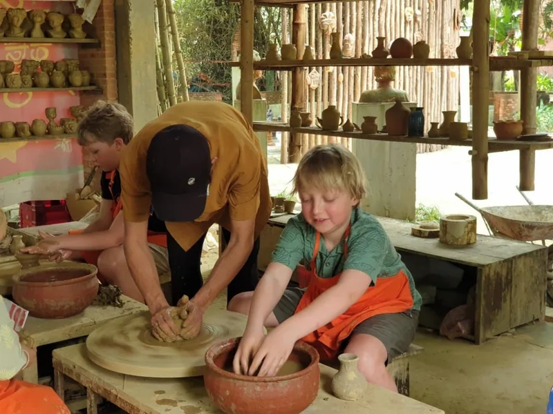 Children learn to shape clay on a pottery wheel with a local artisan at a traditional craft village in Hoi An.