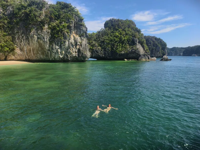 Two swimmers float in turquoise water beneath limestone karsts in Lan Ha Bay near Cat Ba Island.