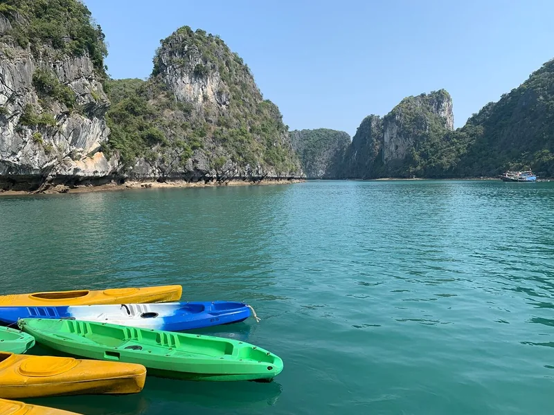 Colorful kayaks float on turquoise water among towering limestone karsts in Lan Ha Bay.