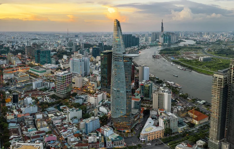 Aerial sunset view of Ho Chi Minh City skyline with the Bitexco tower rising beside the winding Saigon River.