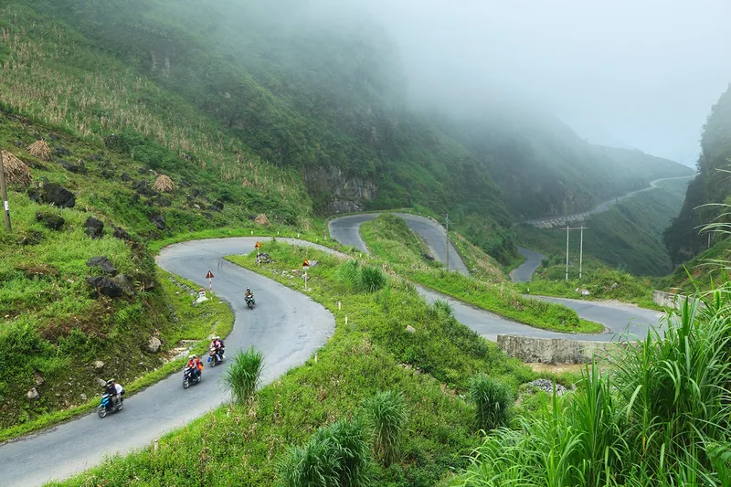 Motorbikes wind through the hairpin turns of Tham Ma Pass amid misty green mountains in Ha Giang.