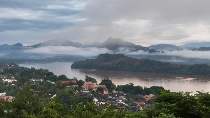 Misty mountains overlook the Mekong River and rooftops of Luang Prabang at dawn.